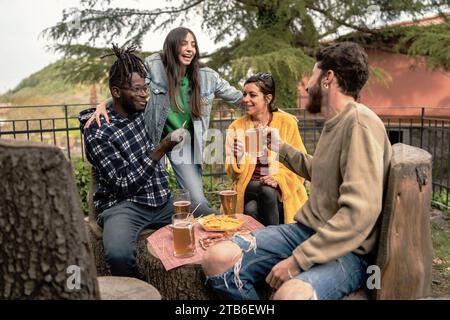 Un gruppo eterogeneo di amici condivide drink e Risate mentre si gode un ritrovo informale in un parco naturale. Foto Stock