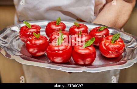 Un primo piano di pomodori ripieni fatti in casa guarniti con foglie di menta strappate disposti su un vassoio di metallo collocato in un'accogliente cucina a casa Foto Stock