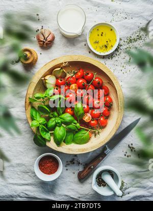 Cucina italiana con pomodori freschi e foglie di basilico sul tavolo con altri ingredienti, vista dall'alto Foto Stock