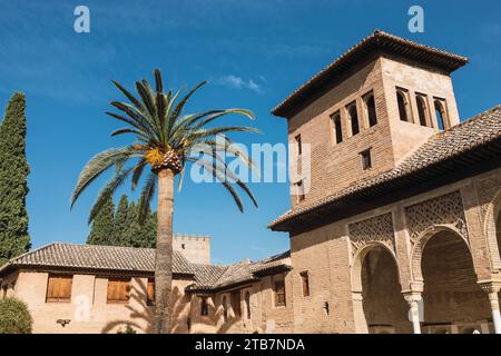 Low angle view of historic Torre de las Damas tower and trees against blue sky located at Alhambra complex in Grenada, Spain during sunny day Foto Stock