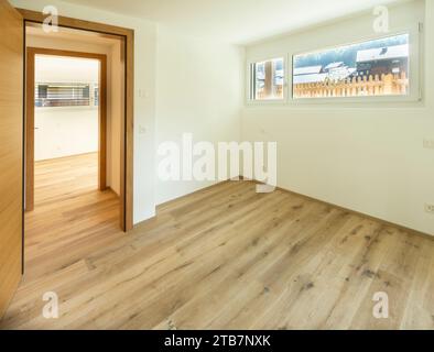 Una sala vuota con luce naturale, pavimento in laminato di legno e una porta di legno aperta che conduce ad un'altra sala. Foto Stock