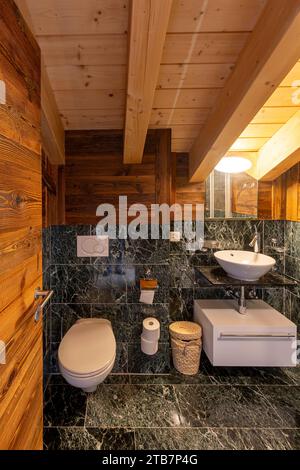 Bagno moderno che combina elementi rustici in legno ed eleganti sanitari, con pareti in marmo e pavimento piastrellato. Foto Stock