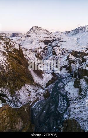 Vista aerea di una catena montuosa innevata di Thormork con un fiume tortuoso che attraversa terreni accidentati nelle Highlands islandesi. Foto Stock