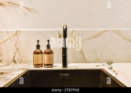 Dispenser di sapone collocati da lavabo nero in bagno piastrellato bianco nell'appartamento contemporaneo Foto Stock