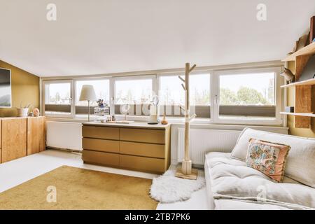 Comodo divano con prodotti di bellezza su comò in legno collocato da grandi finestre luminose nel moderno soggiorno Foto Stock