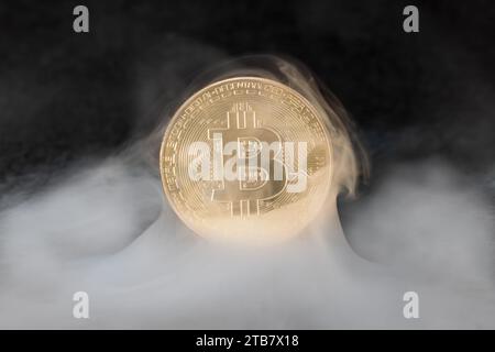 Un singolo Bitcoin giacente in un'atmosfera nebbiosa, con la parola Bitcoin visibile sullo sfondo Foto Stock