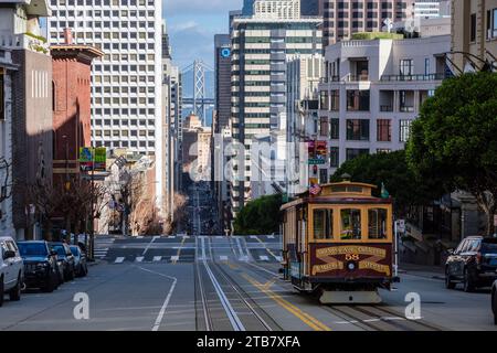 Una funivia che scende lungo California Street verso Powell Street con l'Oakland Bay Bridge sullo sfondo, San Francisco, California, USA Foto Stock
