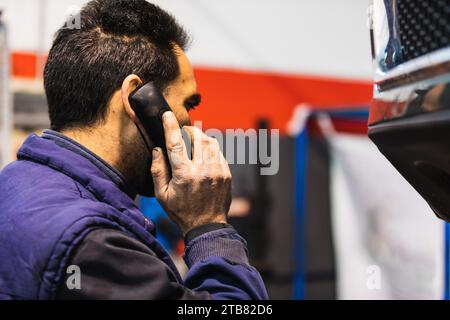 Meccanico che parla al telefono cellulare nella sua officina Foto Stock
