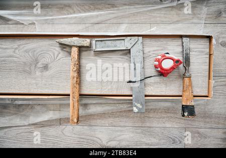 Righello in metallo, martello e metro su tavola in legno laminato. Strumenti e strumenti per la riparazione di edifici per l'installazione di pavimenti in laminato, lavori di costruzione e ristrutturazione di abitazioni. Foto Stock