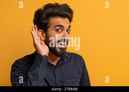 Curioso e allegro indiano che tiene per mano l'orecchio cercando di sentire qualcosa Foto Stock