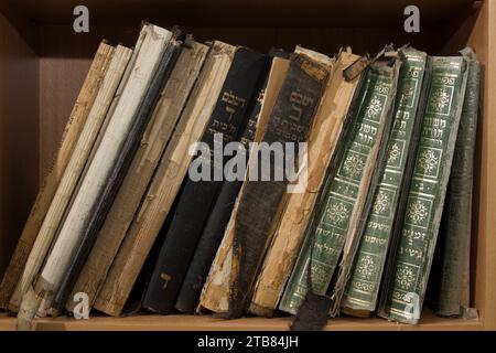 Libri sacri ebraici con rilegatura in pelle polverosa, usurata e sbiadita impilati in posizione verticale su uno scaffale della biblioteca. Foto Stock