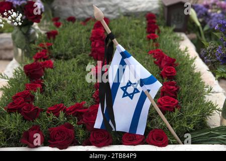 Una bandiera dello Stato di Israele poggia su una tomba di un soldato caduto coperto di fiori colorati nel cimitero militare di Har Herzl a Gerusalemme Foto Stock