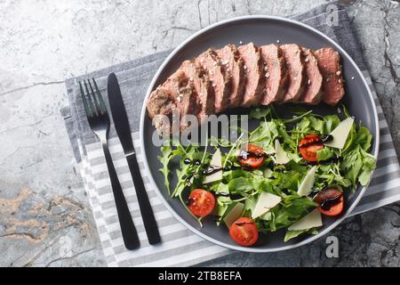 Piatto principale italiano tradizionale tagliata di manzo, bistecca tenera, rucola, pomodori ciliegini, scaglie di Grana Padano, riduzione balsamica da vicino su un piatto su T. Foto Stock