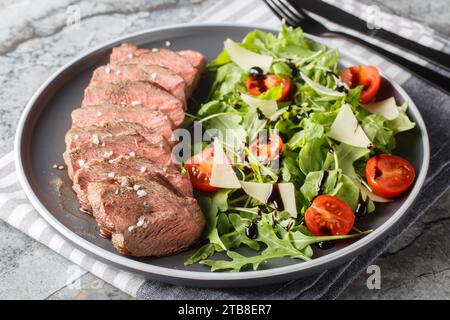 Piatto principale italiano tradizionale tagliata di manzo, bistecca tenera, rucola, pomodori ciliegini, scaglie di Grana Padano, riduzione balsamica da vicino su un piatto su T. Foto Stock