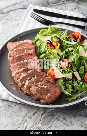 Tagliata di manzo bistecca di manzo all'italiana servita con rucola, pomodori ciliegini e parmigiano da vicino in un piatto sul tavolo. Verticale Foto Stock