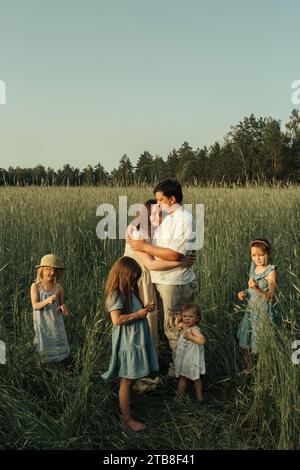 Una grande famiglia composta da padre, madre e quattro figlie si trova in un campo verde in estate. Ritratto di famiglia. Foto Stock