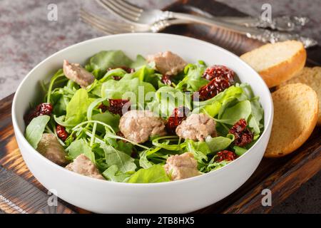Deliziosa insalata di fegato di merluzzo con rucola e pomodori secchi serviti con toast da vicino in una ciotola sul tavolo. Orizzontale Foto Stock