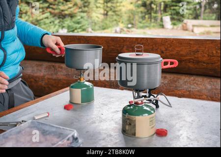 Preparazione turistica di pentola sul bruciatore con gas in scatola nel campeggio nella foresta Foto Stock