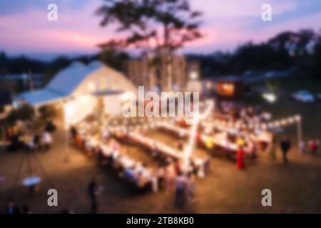 Scena sfocata di catering illuminato che celebra con tavolo da pranzo e ospiti al tramonto Foto Stock