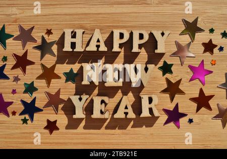 Felice anno nuovo, parole in lettere alfabetiche di legno circondate da coriandoli casuali isolati su fondo di legno Foto Stock