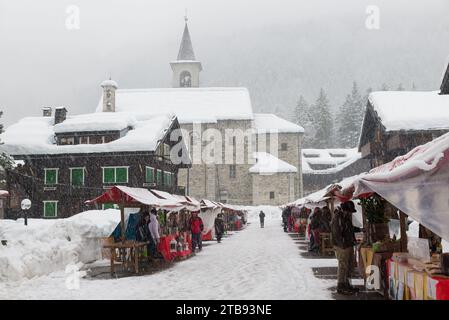 Onde fredde e neve in Europa in un villaggio alpino di montagna. La gente è alla ricerca di regali di Natale tra le bancarelle sotto la neve pesante, Macugnaga Italia Foto Stock