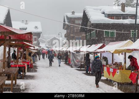 Onde fredde e neve in Europa in un villaggio alpino di montagna. La gente è alla ricerca di regali di Natale tra le bancarelle sotto la neve pesante, Macugnaga Italia Foto Stock