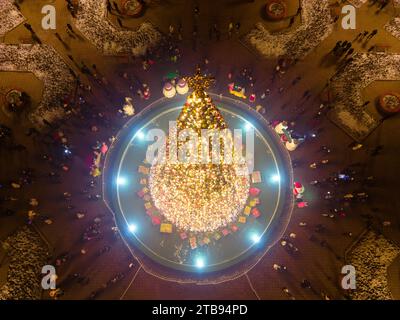 Vista aerea dall'alto verso il basso delle luci illuminate su un albero di Natale in una piazza piena di persone Foto Stock