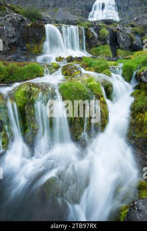 Due piccole cascate e la più grande cascata Dynjandi sullo sfondo; l'Islanda Foto Stock