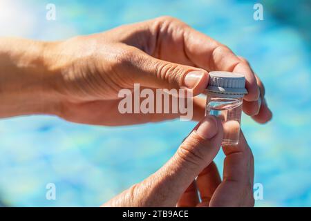 Mani ravvicinate che chiudono una fiala d'acqua per l'analisi del pH vicino a una piscina di un hotel Foto Stock