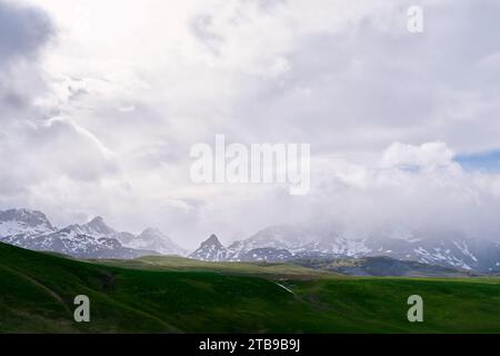 La nebbia sulle montagne innevate scende verso una valle verde Foto Stock