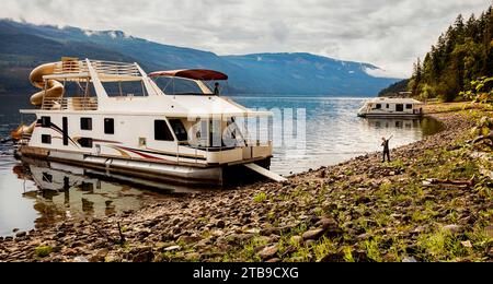 Una famiglia che si gode una vacanza in casa galleggiante mentre è parcheggiata sulla riva del lago Shuswap; lago Shuswap, British Columbia, Canada Foto Stock