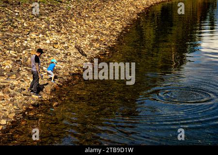 Un padre e la sua giovane figlia saltano rocce su una costa mentre sono in vacanza; il lago Shuswap, British Columbia, Canada Foto Stock