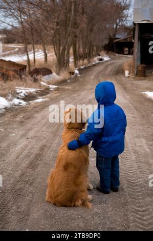 Giovane ragazzo si trova in una strada ghiaiosa con un Golden retriever; Cortland, Nebraska, Stati Uniti d'America Foto Stock