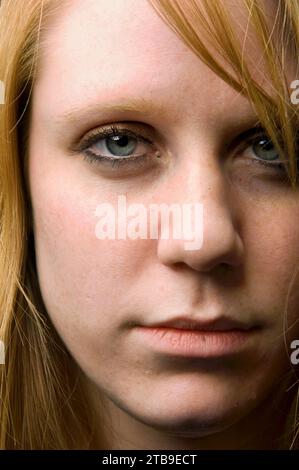 Primo piano del viso di una giovane donna, con lunghi capelli biondi fragole, occhi blu e un'espressione seria; studio Foto Stock