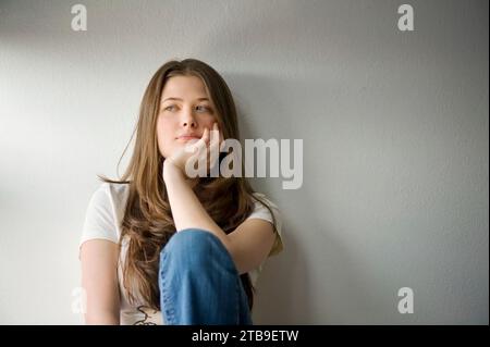 Ritratto di una giovane donna adulta seduta e appoggiata su un muro bianco; Fairbanks, Alaska, Stati Uniti d'America Foto Stock