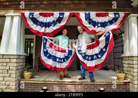 Due uomini appendono striscioni patriottici sul portico di una casa; Lincoln, Nebraska, Stati Uniti d'America Foto Stock