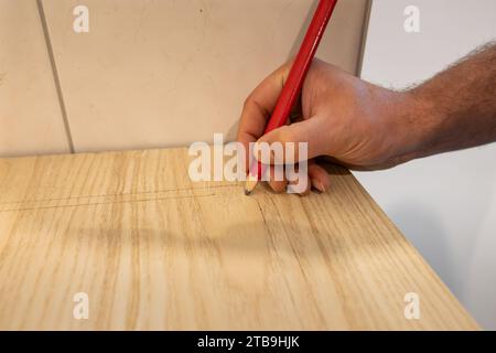 Contrassegnare un piano di lavoro con una matita di piombo. Il falegname prepara la parte in legno per vederla. Costruire una nuova cucina in un appartamento. Foto Stock