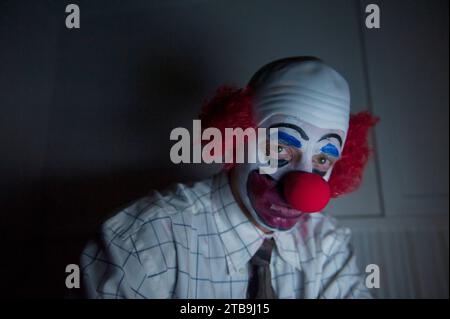 Ritratto ravvicinato di un clown seduto da solo in una stanza buia con maglietta e cravatta; Lincoln, Nebraska, Stati Uniti d'America Foto Stock