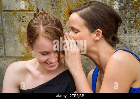 Due giovani donne in formalwear si sussurrano segreti l'una all'altra; Lincoln, Nebraska, Stati Uniti d'America Foto Stock