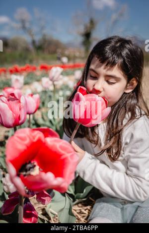 vista ravvicinata di una ragazza in abito bianco che odora un grande fiore seduto in un campo di tulipani Foto Stock