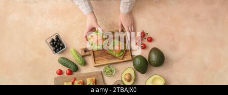 Donna con gustosi panini con guacamole e salmone su sfondo grunge, vista dall'alto Foto Stock