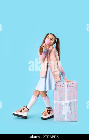 Ragazza alla moda con confezione regalo che soffiano gomma da bolla su sfondo blu Foto Stock