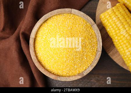 Farina di mais cruda in ciotola e pannocchia di mais su un tavolo di legno, vista dall'alto Foto Stock