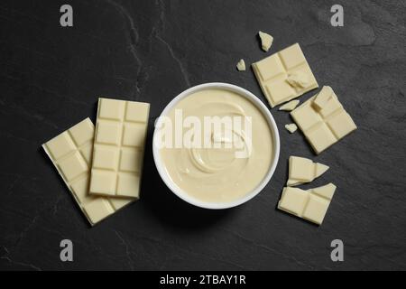 Gustosa pasta di cioccolato bianco in ciotola e pezzi sul tavolo nero, vista dall'alto Foto Stock