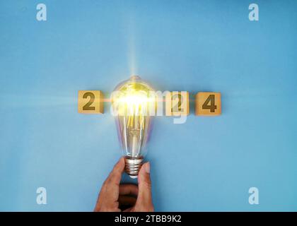 Calendario 2024 brillante, lampadina di tendenza creativa tenuta da un uomo d'affari che brilla in modo luminoso. rete digitale e contesto di lusso. Buon anno 20 Foto Stock