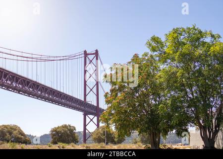 Vista diurna dell'iconico Ponte 25 de Abril di Lisbona: Un paesaggio orizzontale girato da terra, che cattura il maestoso Ponte sospeso Rosso Foto Stock