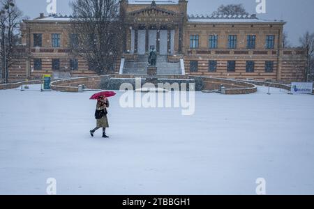 Schwerin, Germania. 5 dicembre 2023. Una donna cammina attraverso il Vecchio Giardino di fronte al Museo di Stato in una nevicata. Le forti nevicate in luoghi e temperature al di sotto dello zero ostacolano il traffico nella Germania settentrionale. Credito: Jens Büttner/dpa/Alamy Live News Foto Stock