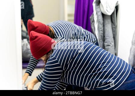 una donna di mezza età prova una giacca e un cappello nel camerino del punto di prelievo Foto Stock