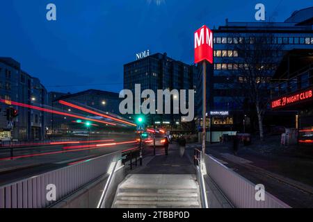 Ingresso alla stazione della metropolitana di Sörnäinen dopo il tramonto con i sentieri delle luci di coda degli autobus rossi lungo Hämeenkatu a Helsinki, Finlandia Foto Stock