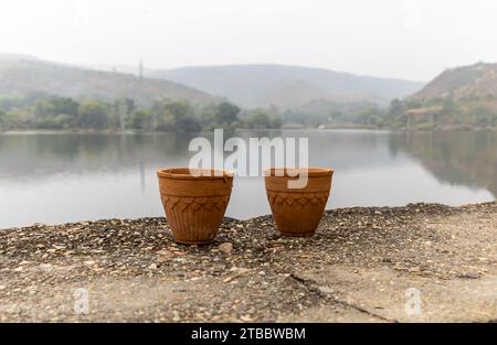 tè caldo servito in tradizionale tazza di ceramica senza mani in argilla con un paesaggio confuso del lago di montagna Foto Stock